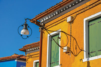 Lamp stuck in colored wall and windows with wooden blinds closed on a sunny day in burano, italy.