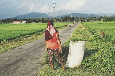 Rear view of woman with crops standing at roadside in farm