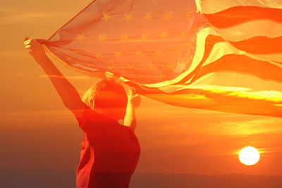 Double exposure image of boy holding american flag and orange sky