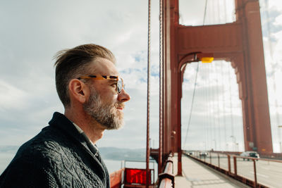 Profile portrait of adult man with beard standing on the golden gate bridge during cloudy weather