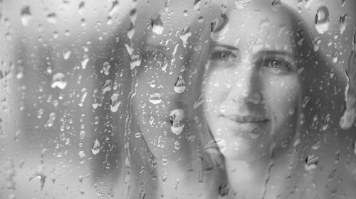 Woman looking through wet window in rainy season