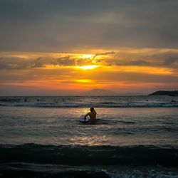 Silhouette man sitting on beach against sky during sunset
