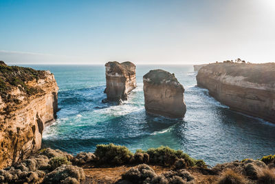 Scenic view of rock formations in sea against clear sky during sunset