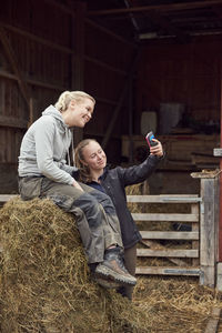 Young woman taking selfie with sister sitting on hay bale