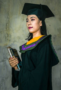 Smiling young woman using smart phone while standing against wall