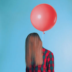 Woman with balloon standing against blue wall