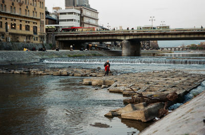 Man on bridge over river in city against sky