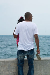 Rear view of man standing in sea against sky