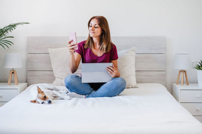 Woman with dog using phone while sitting on bed