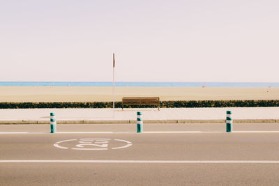 Scenic view of beach in front of road against sky on sunny day