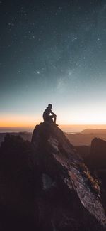 Silhouette man sitting on rock against sky at night