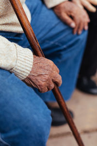 Anonymous senior person holding cane while sitting on park bench