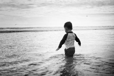 Rear view of boy standing in sea against cloudy sky