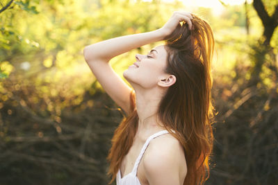 Side view of young woman standing against plants