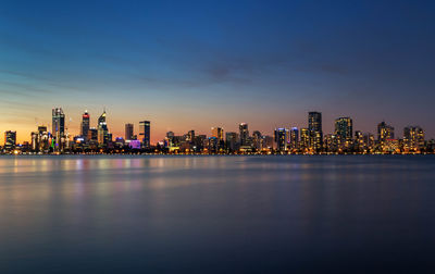 Sea by illuminated modern buildings in city against sky