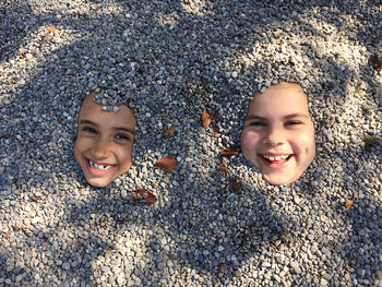 High angle portrait of smiling girls buried in  pebbles