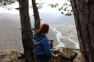 Side view of woman sitting by tree trunk in forest