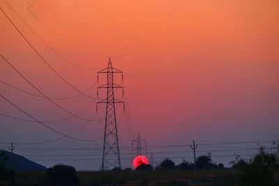 Silhouette of electricity pylon against cloudy sky during sunset