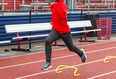 High school boy running over yellow mini hurdles on a track during track and field practice.