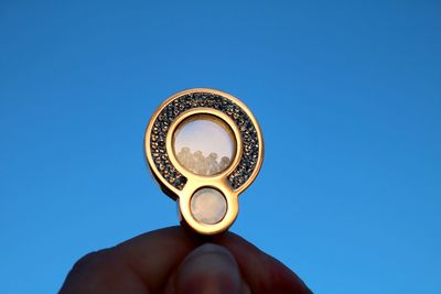 Low angle view of hand holding metal against clear blue sky