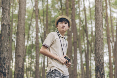 Young man standing by tree trunk in forest