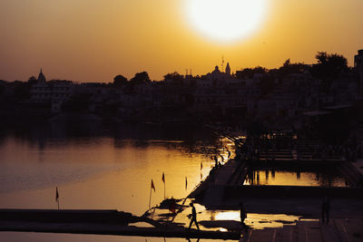 Scenic view of river by silhouette city against orange sky