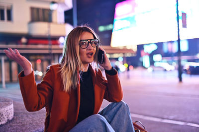 Young woman using mobile phone while sitting in city