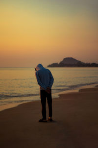 Rear view of woman standing at beach against sky during sunset