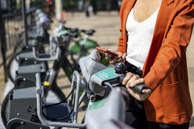 Hand of businesswoman renting electric bicycle through smart phone