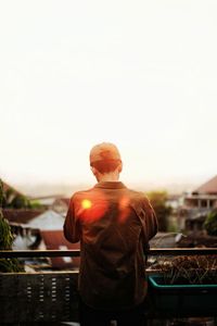 Rear view of man standing by railing against sky during sunset