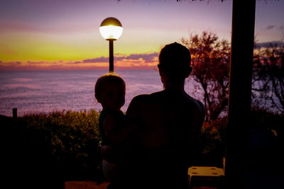 Rear view of silhouette couple standing against sky during sunset