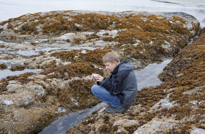 Teenage boy photographing tidal pool at beach