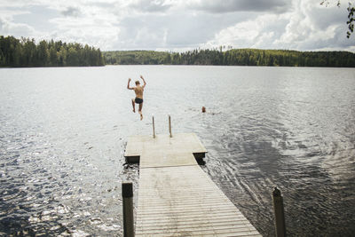 Rear view of man swimming on lake against sky