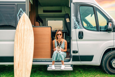Woman sitting with her dog at the door of her camper van during a trip