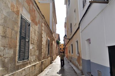 Rear view of man walking on alley amidst buildings