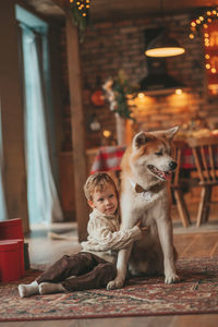 Candid authentic happy little boy in knitted beige sweater hugs dog with bow tie at home on xmas