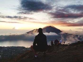 People looking at mountains against sky during sunset