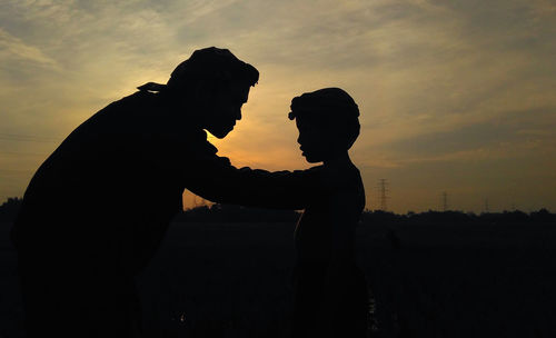 Silhouette father and son against sky during sunset