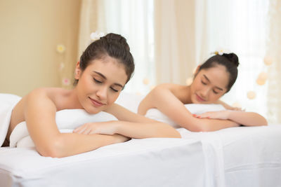 Young female friends lying with eyes closed on massage tables in spa