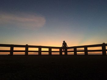 Silhouette man sitting on railing against sky during sunset