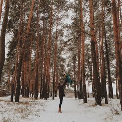 Side view of father picking up son while standing on snow covered forest