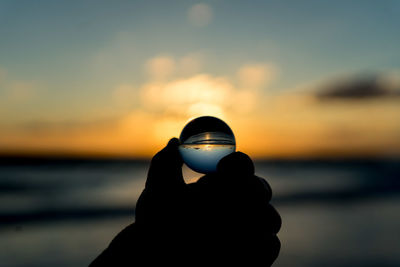 Silhouette person holding sea against sky during sunset