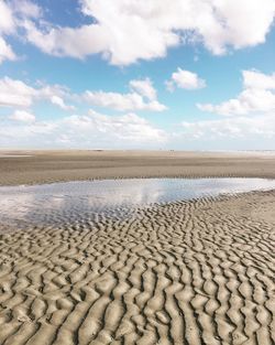 Idyllic shot of water on sand at beach against sky