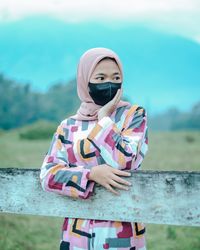 Girl touching face while standing near fence