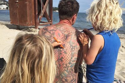 Children coloring tattoo of father at beach