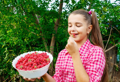 Girl eating berries while standing against plants