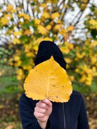 Person holding dry leaf in front of face while standing against trees