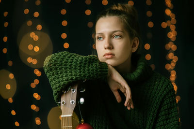 A beautiful teenager girl dreamily looks to the side, leaning on the neck of a guitar