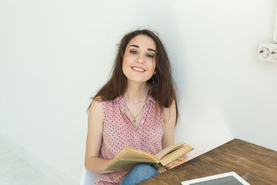 Portrait of beautiful young woman reading book against wall