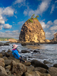 Rear view of woman sitting on rock by sea against sky